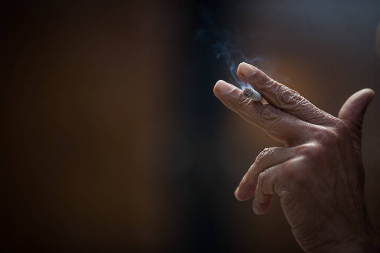 Aparece na imagem apenas a mão de um homem e um cigarro apoiado entre seus dedos