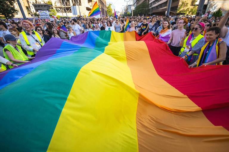 Manifestantes seguram grande bandeira com arco-íris, símbolo da comunidade LGBTQIA+, em marcha