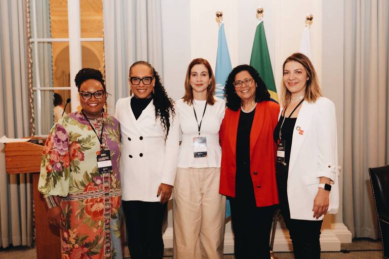 Foto mostra cinco mulheres abraçadas lado a lado, sorrindo em direção à câmera