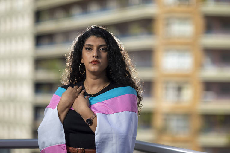 Mulher está coberta com bandeira branca, rosa e azul.