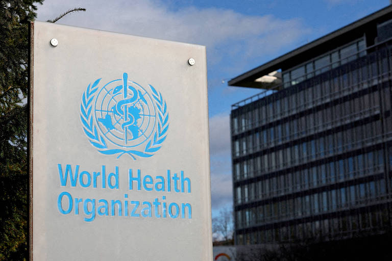 A imagem mostra um sinal da Organização Mundial da Saúde (OMS) em um painel de pedra. O logotipo da OMS, que inclui um símbolo de um bastão de Asclépio cercado por uma coroa de louros, está em azul. Ao fundo, há um edifício moderno com janelas de vidro e céu parcialmente nublado.