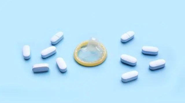 Foto de uma camisinha com comprimidos ao redor