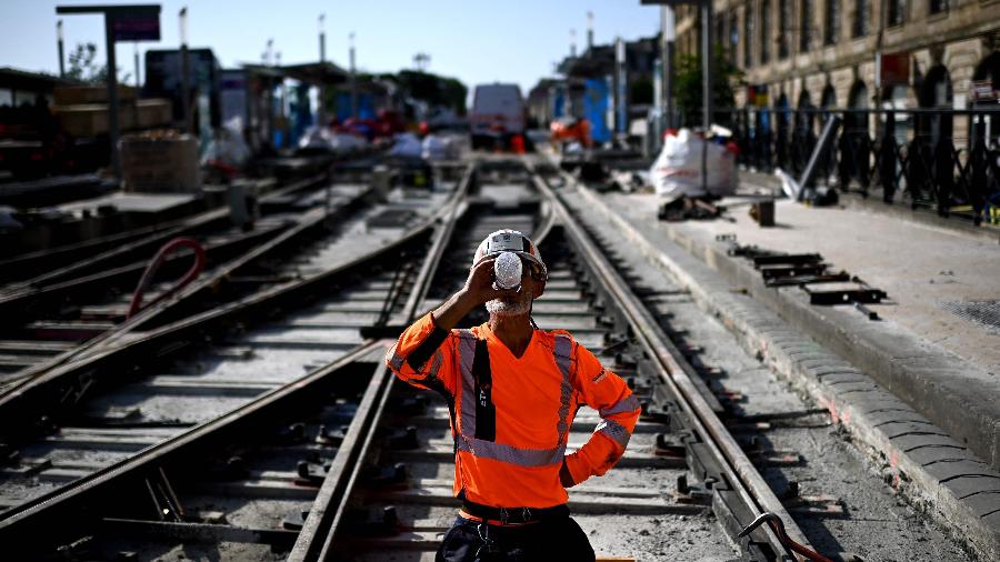 Trabalhador bebe água para se refrescar enquanto trabalha em um canteiro de obras de linhas de bonde durante uma onda de calor em Bordeaux, sudoeste da França